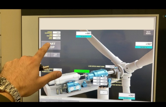 A person points at a computer screen displaying a wind turbine simulator interface, showcasing bespoke equipment in use.