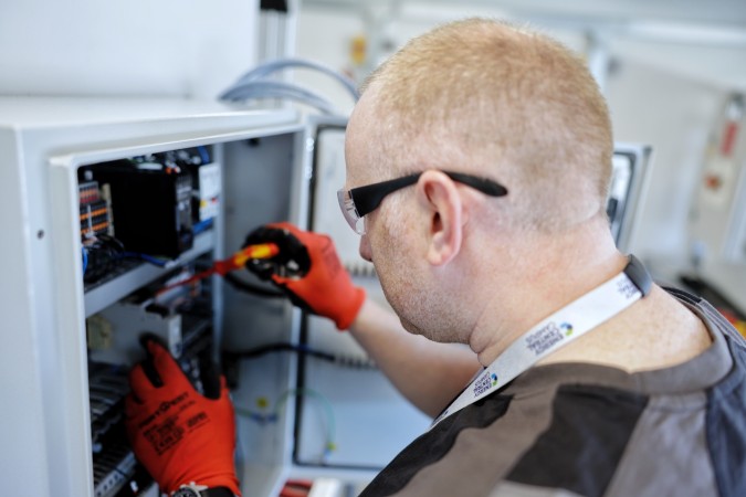 A man in a black shirt and red gloves works inside an electrical cabinet.