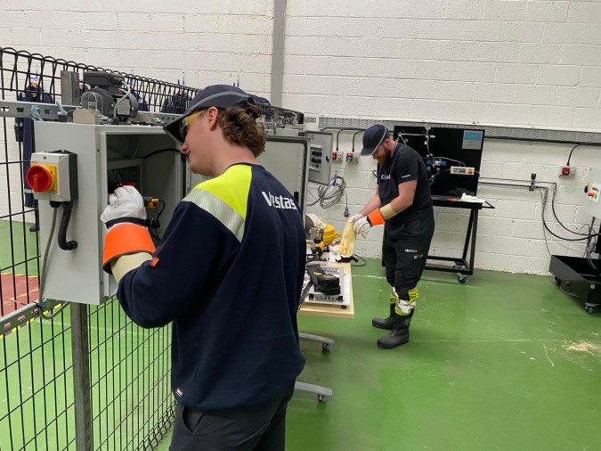 Two wind turbine technicians practice machine operations during a training session in a practical environment.