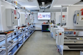 The WTS electrical training room at Energy Central, lined with control panel rigs and workbenches, WTS logo displayed on screen.
