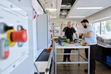 Two men, an instructor and a student, work together in a workshop during an electrical training course.