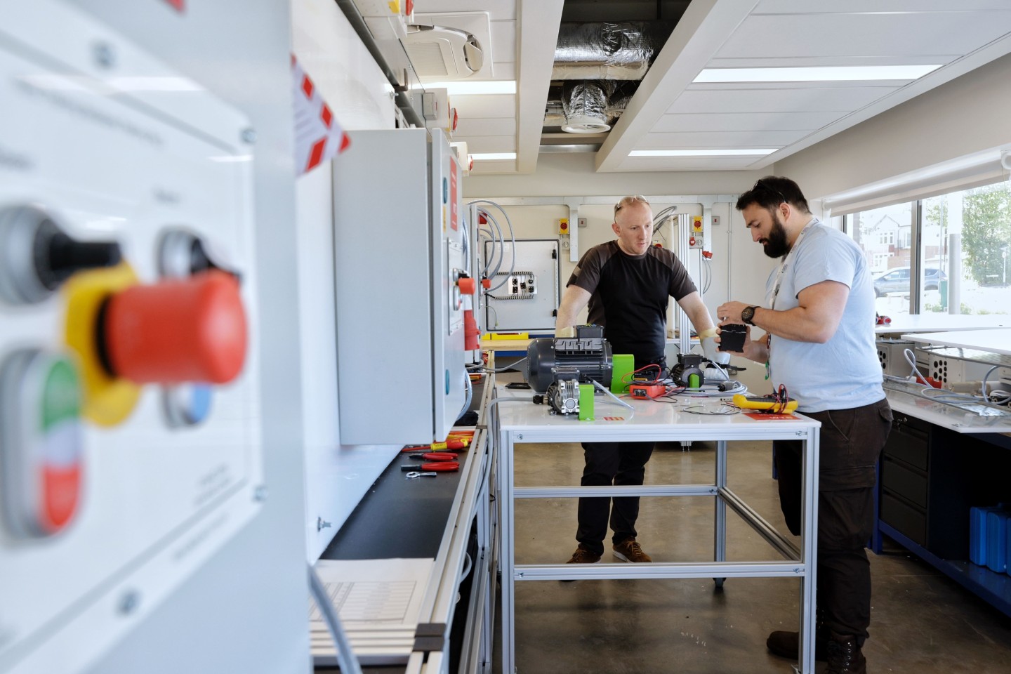 An image of a technical instructor teaching a technician on an electrical course in front of equipment. 