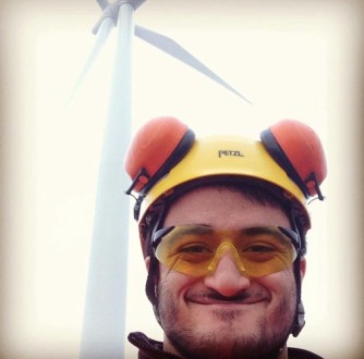 An 18 year old Dominic Connolly wearing PPE (hard hat and ear defenders) in front of a wind turbine on his first site visit as a Siemens wind turbine technician apprentice.