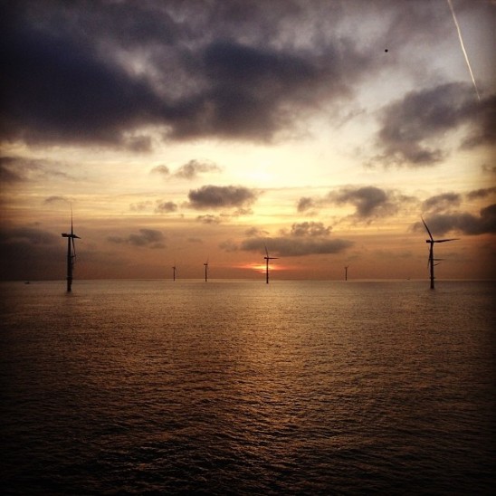 An image of a wind farm offshore at sunset.